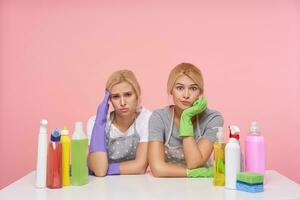 interior foto do bonita jovem cabeça branca senhoras guardando elevado mãos em dela cabeça enquanto olhando às Câmera com cansado rostos, sentado sobre Rosa fundo com garrafas do família produtos químicos