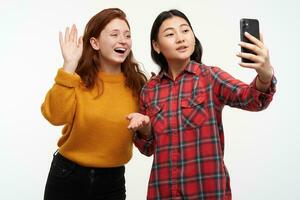 pessoas e estilo de vida conceito. dois fofa garotas. vestindo amarelo suéter e xadrez camisa. menina introduzir dela amigo para pais com vídeo chamar. fazer selfie. ficar de pé isolado sobre branco fundo foto