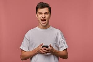 uma homem dentro uma branco t - camisa segurando uma célula telefone foto