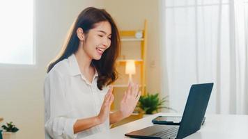 mulher de negócios asiáticos jovem usando videochamada de laptop falando com o casal enquanto trabalhava em casa na sala de estar. auto-isolamento, distanciamento social, quarentena para coronavírus no próximo conceito normal. foto