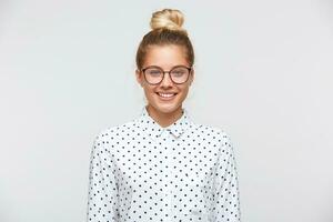 retrato do alegre lindo jovem mulher com pão desgasta polca ponto camisa e óculos sente confiante e parece para a Câmera isolado sobre branco fundo foto