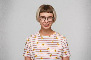 retrato do alegre atraente jovem mulher desgasta listrado t camisa e óculos sente feliz e rindo isolado sobre branco fundo foto