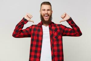 fechar acima retrato do uma alegre feliz barbudo homem dentro xadrez camisa aperto punhos e apontando polegares em ele mesmo gostar vencedora com olhos fechadas dentro prazer, isolado sobre branco fundo foto