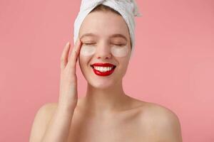 retrato do jovem desfrutando mulher depois de chuveiro com uma toalha em dela cabeça, com remendos e vermelho lábios, toques face, carrinhos sobre Rosa fundo. foto