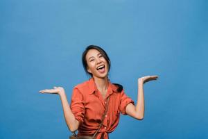 retrato de uma jovem asiática sorrindo com uma expressão alegre, mostra algo incrível no espaço em branco em um pano casual e olhando para a câmera isolada sobre fundo azul. conceito de expressão facial. foto