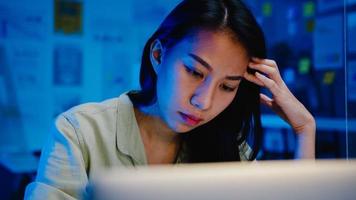 mulheres asiáticas freelance usando laptop trabalham duro no novo escritório normal. trabalhar em casa sobrecarga à noite, trabalhar remotamente, auto-isolamento, distanciamento social, quarentena para prevenção do vírus corona.
