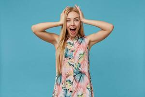 retrato do espantado jovem Loiras mulher com casual Penteado posando sobre azul fundo, guardando Palmeiras em dela cabeça e olhando alegremente às Câmera com Largo boca aberto foto