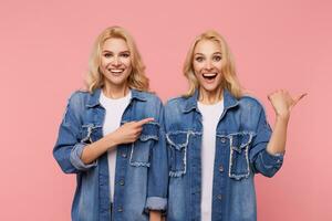 alegre jovem adorável cabeça branca grandes cabelos senhoras sorridente alegremente enquanto mostrando a parte, de lado com elevado mão, isolado sobre Rosa fundo dentro azul jeans casacos foto