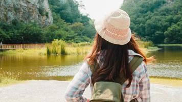 alegre jovem viajante asiática com mochila caminhando no lago de montanha. adolescente coreana desfrutar de sua aventura de férias sentindo feliz liberdade. viajar de estilo de vida e relaxar no conceito de tempo livre. foto