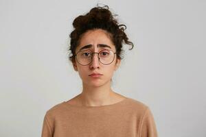 retrato do triste chateado georgiano jovem mulher com encaracolado cabelo desgasta bege estacionar e óculos sente infeliz e frustrado isolado sobre branco fundo foto