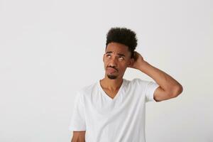 horizontal foto do jovem confuso Sombrio esfolado morena cara com barba segurando mão em dele occipital enquanto olhando pensativamente para cima, isolado sobre branco fundo