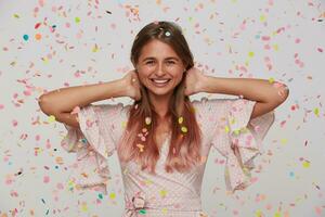 fechar-se do feliz bonita jovem mulher com grandes tingido pastel Rosa cabelo desgasta polca ponto Rosa vestir a comemorar aniversário e tendo Diversão sobre branco fundo com confete foto