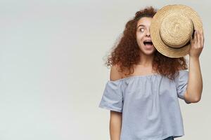 Adolescência garota, feliz olhando mulher com encaracolado gengibre cabelo. vestindo listrado ombros caídos blusa e cobrir metade do dela face com chapéu. assistindo para a esquerda às cópia de espaço, isolado sobre branco fundo foto