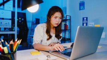 mulheres asiáticas freelance usando laptop trabalham duro no novo escritório doméstico normal. trabalho em casa sobrecarregada à noite, trabalho remoto, auto-isolamento, distanciamento social, quarentena para prevenção do vírus corona. foto
