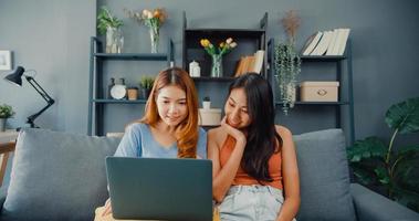 duas mulheres lésbicas da Ásia site juntos no sofá, olhando para a tela do laptop na sala de estar em casa juntos. senhoras de companheiro de quarto de casal feliz desfrutar de compras on-line de navegação na web, conceito de mulher de estilo de vida em casa. foto