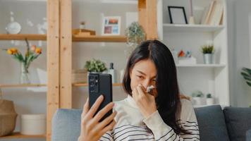 mulher asiática jovem doente segurar medicina sentar no sofá, videochamada com telefone, consultar o médico em casa. garota tomar remédio após ordem do médico, quarentena em casa, conceito de coronavírus de distanciamento social. foto