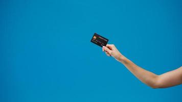 mão de mulher jovem mostra o cartão de crédito para fazer compras online sobre fundo azul no estúdio. copie o espaço para colocar um texto, mensagem para anúncio. área de publicidade, maquete de conteúdo promocional. foto