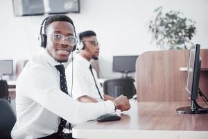Operador de suporte ao cliente afro-americano com fone de ouvido viva-voz trabalhando no escritório foto