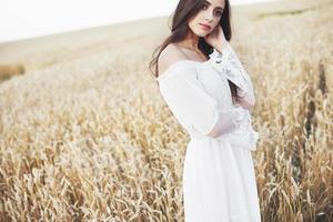 jovem sensível em um vestido branco posando em um campo de trigo dourado
