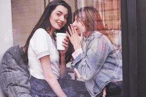 duas belas moças sentadas em um café, bebendo café e tendo uma conversa agradável depois das compras