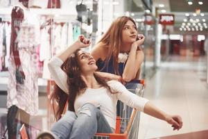 mulheres jovens se divertem com uma cesta de supermercado à noite. jovem atraente passando um tempo juntos no shopping