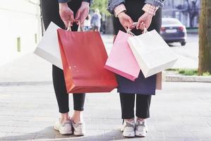 duas jovens carregando sacolas de compras enquanto caminha pela rua após visitar as lojas foto