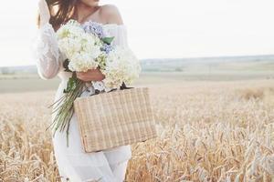 linda garota de vestido branco correndo no campo de trigo de outono ao pôr do sol foto