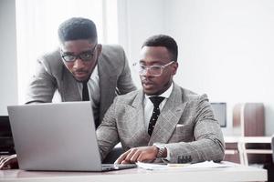 empresário moderno no trabalho. dois executivos confiantes em trajes formais discutindo algo e olhando para o monitor do laptop