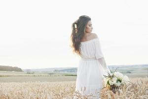 linda garota de vestido branco correndo no campo de trigo de outono ao pôr do sol foto