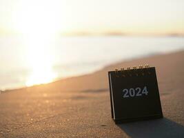 fechar acima 2024 escrivaninha calendário em a de praia dentro a pôr do sol tempo. resolução, meta, Ação, planejamento, e gerir para sucesso negócios. foto