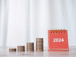 2024 escrivaninha calendário e pilha do moedas. a conceito do salvando dinheiro, financeiro, investimento e o negócio crescendo dentro Novo ano 2024. foto