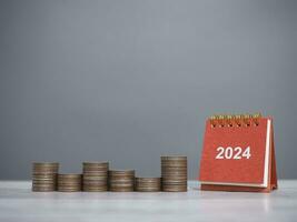 2024 escrivaninha calendário e pilha do moedas. a conceito do salvando dinheiro para financeiro, investimento e o negócio crescendo dentro Novo ano 2024. foto