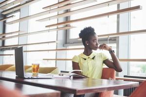 jovem garota afro-americana com cabelo escuro encaracolado pensativa em um café. foto