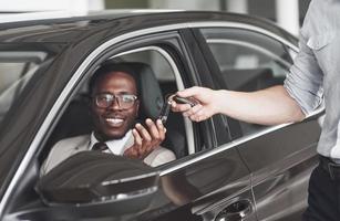 um afro-americano pega as chaves de um carro em uma concessionária. foto