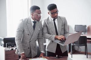 empresário moderno no trabalho. dois executivos confiantes em trajes formais discutindo algo e olhando para o monitor do laptop foto