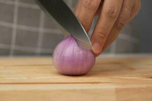 fêmea mão usando faca para fatia fresco vermelho cebola em cortar quadro, fechar-se. chefe de cozinha cortar chalotas usando uma afiado faca em uma de madeira cortar borda. preparando caseiro Comida foto