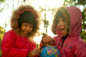 duas lindas garotas asiáticas aprendendo um modelo do mundo no fundo da natureza e luz do sol quente no parque. as crianças aprendem através de atividades lúdicas educativas. Dia da Terra. dia Mundial do Meio Ambiente. foto