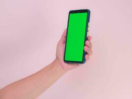 humano mão segurando Móvel Smartphone com verde tela dentro vertical posição isolado em Rosa fundo. recorte caminho foto