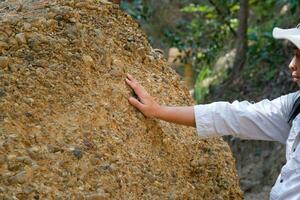 fêmea geólogo com mochila explorando natureza trilha dentro floresta e analisando Rocha ou cascalho. pesquisadores coletar amostras do biológico materiais. de Meio Ambiente e ecologia pesquisar. foto