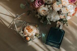 Casamento detalhes fotografado a partir de acima em uma cinzento têxtil fundo, masculino perfume, nupcial ramalhete, Casamento argolas dentro uma vidro caixa decorado com flores foto