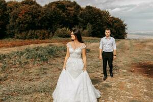 a Casamento casal é caminhando dentro a montanhas em a fundo do a outono floresta, a noiva é dentro a primeiro plano foto