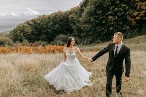 uma romântico conto de fadas casal do recém-casados estão caminhando dentro uma campo às pôr do sol, atrás samambaia folhas. a noiva é dentro uma branco Casamento vestir, a noivo é dentro uma Preto clássico terno e uma branco camisa foto