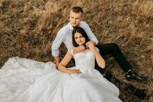 a noiva e noivo estão deitado em a seco Relva e abraçando, uma mulher dentro uma branco Casamento vestir. lindo outono Casamento foto. foto