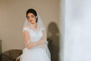 retrato do a noiva dentro dela Casamento vestir debaixo uma véu dentro dela quarto de a janela. foto