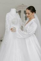 à moda noiva com Casamento Penteado e Maquiagem dentro branco roupão em pé perto dela Casamento vestir. foto