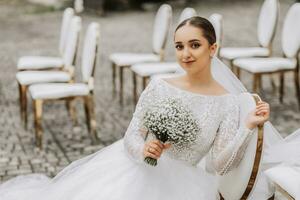 noiva com uma ramalhete do flores senta e poses em branco cadeiras com ouro arestas depois de a Casamento cerimônia foto