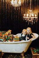 alegre Natal e feliz feriados. alegre menina e Garoto dentro uma banho com Natal presentes dentro ouro invólucro. crianças estão tendo Diversão. amoroso família com presentes dentro a sala. foto