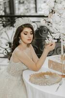 glamouroso retrato do uma menina às uma mesa com uma decorativo dourado placa, uma noiva dentro uma Casamento vestir e uma coroa em dela cabeça foto