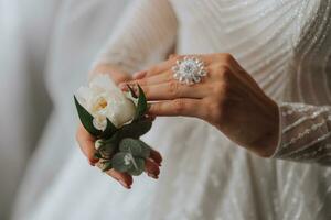 detalhes Casamento acessórios. a noiva é segurando uma branco rosa, uma lindo Casamento anel com uma cristal em dela mão. cortada foto. lindo mãos foto