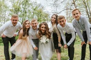 Casamento andar dentro a floresta. noivas e seus amigos pose contra a fundo do a floresta. uma ampla grupo do pessoas estão tendo Diversão às seus amigos' Casamento foto